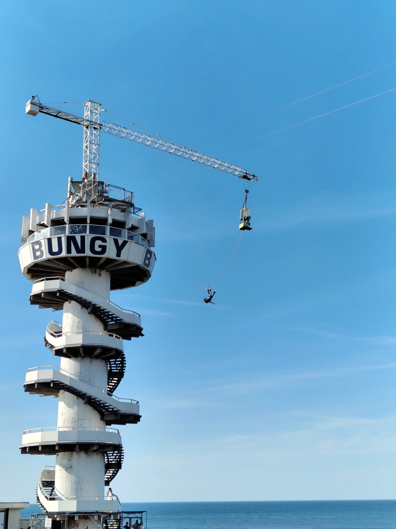Photo of a bungee jump tower with a person mid-jump over the ocean under a clear blue sky, taken with the 2x setting on a Fairphone Gen. 6